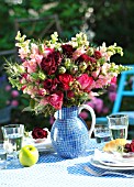 BOUQUET OF ROSES IN A BLUE JUG ON A SET TABLE WITH AN APPLE