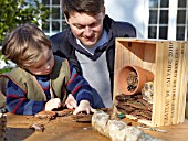 INSECT HOUSE BUILDING PROJECT WITH FATHER AND SON.  FILLING GAPS IN THE BOX WITH BARK.  STEP 17