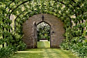 PERGOLA WALK WITH TRAINED PEARS AND VIEW THROUGH DOOR AT OZLEWORTH PARK, GLOUCESTERSHIRE