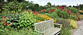 THE LANHYDROCK GARDEN WITH WOODEN BENCH AND BORDERS OF HERBACEOUS PERENNIALS IN HOT COLOURS AT WOLLERTON OLD HALL
