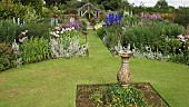 Stone sundial in lawn with twin borders of many colours and varieties of herbaceous perrenials