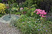 Sundial set in gravel area with borders of mixed herbaceous perennials