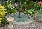 Sundial set in gravel area with borders of mixed herbaceous perennials