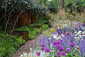 TELEGRAPH GARDEN,  DES. TOM STUART SMITH. PATHWAY & RUSTED STEEL WATER TANKS WITH VIBURNUM RHYTIDOPHYLLUM TO LEFT; ALLIUMS,  NEPETA RACEMOSA WALKERS LOW,  STACHYS BYZANTINA & STIPA GIGANTEA. CHELSEA 2006