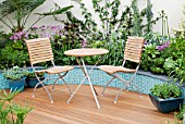 TABLE & CHAIRS ON DECKING WITH CERAMIC TILE RAISED BORDERS BEHIND. MITIE GARDEN,  DES. JO PENN. INC.