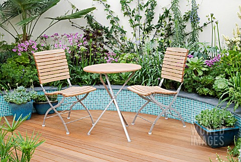 TABLE__CHAIRS_ON_DECKING_WITH_CERAMIC_TILE_RAISED_BORDERS_BEHIND_MITIE_GARDEN__DES_JO_PENN_INC