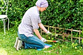 Woman cutting a lawn edge near a border. She is using a kneeling mat