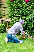 Woman cutting a lawn edge near a border. She is using a kneeling mat