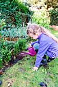 Little girl making a cutting from Buxus, watering in