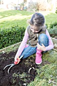 Young girl loosening the soil of the squarefoot kitchen garden