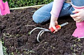 Young girl loosening the soil of the squarefoot kitchen garden