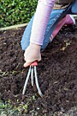 Young girl loosening the soil of the squarefoot kitchen garden