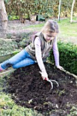 Young girl loosening the soil of the squarefoot kitchen garden