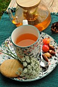 Lime infusion in a cup and plate with plant motifs, glass teapot, Napoleon cherries and Brazil nuts