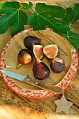 Black figs, (Ficus carica) on a wooden plate, fig leaves as decoration, summer fruits