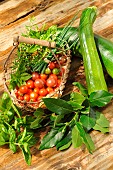 Garden harvest of cherry tomatoes (Solanum lycopersicum), courgettes (Cucurbita pepo), basil (Ocimum basilicum), bay leaves (Laurus nobilis), chives (Allium schoenoprasum) and rosemary (Salvia rosmarinus)