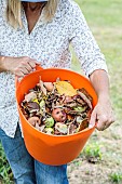 Woman holding a container for cleaning the orchard: damaged, worm-eaten fruit, diseased leaves...