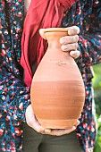 Woman holding an oyas, or watering jar, containing water: the boundary is clearly visible from the outside.