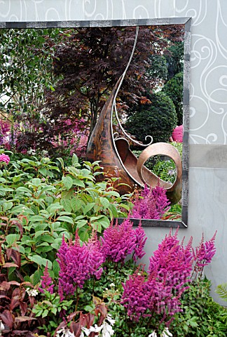ASTILBE_CHINENSIS_VISION_IN_RED_GROWING_BESIDE_METAL_SCULPTURE_REFLECTED_IN_MIRROR_BEHIND