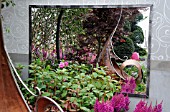 ASTILBE CHINENSIS VISION IN RED GROWING BESIDE METAL SCULPTURE REFLECTED IN MIRROR BEHIND