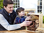 INSECT HOUSE BUILDING PROJECT WITH FATHER AND SON.  PLACING BAMBOO BUNDLE INTO BOX.  STEP 31