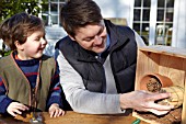 INSECT HOUSE BUILDING PROJECT WITH FATHER AND SON.  PLACING BOUND AND TIED STICKS IN BOX.  STEP 15