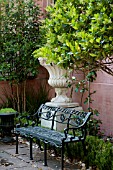 ORNATE BLACK CAST IRON GARDEN BENCH WITH URNS IN GARDEN COURTYARD