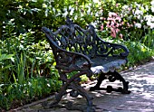 ORNATE IRON BENCH ON BRICK PATH IN SPRING GARDEN