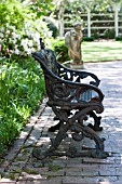 ORNATE IRON BENCH AND STONE STATUE ON BRICK PATH IN SPRING GARDEN
