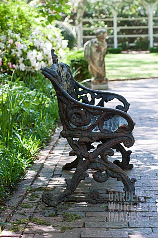 ORNATE_IRON_BENCH_AND_STONE_STATUE_ON_BRICK_PATH_IN_SPRING_GARDEN