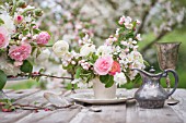 MALUS X EVERESTE WITH OUTDOOR TABLE SET UNDER APPLE BLOSSOMS AND DECORATED WITH FLORAL ARRANGEMENTS OF RANUNCULUS AND ROSES