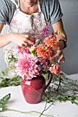 FLORAL DESIGNER ARRANGING BOUQUET WITH ZINNIA, DAHLIA, ROSE, SNAPDRAGON AND OTHER SUMMER FLOWERS