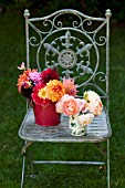 MIXED DAHLIAS IN RED BUCKET WITH DAVID AUSTIN ROSES IN TOILE VASE ON ORNATE IRON GARDEN CHAIR