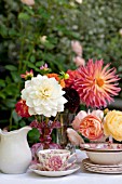 MIXED DAHLIAS AND ROSES IN VASES ON OUTDOOR GARDEN TABLE WITH TEA AND ROSES