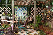 OUTDOOR PATIO GARDEN WITH TRELLIS PERGOLA, QUILT WALL HANGING, TILE AND MOSS FLOOR.