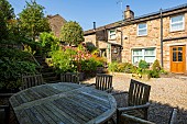 A wooden dining table and chairs in a sunny multi level garden in the Yorkshire Dales.  Stone steps lead to the upper levels of this stepped garden.  A hydrangea blooms in a large pot, and montbretia is a colourful background in early September.