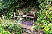 A shady garden spot in a private garden in the Yorkshire Dales. A wooden two seater bench is a comfortable spot for reading or relaxing.