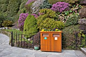 SPRING FLOWERS DECORATE A RUBBISH BIN AGAINST A BACKGROUND OF HEATHERS AND CONIFERS AT BUTCHART GARDENS, BRITISH COLUMBIA, CANADA