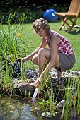 LADY CHECKING POND WATER TEMPERATURE WITH THERMOMETER