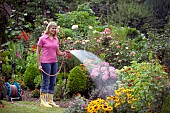 WOMAN WATERING FLOWERS IN GARDEN BED