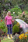 WOMAN WATERING FLOWERS IN GARDEN BED