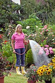 WOMAN WATERING FLOWERS IN GARDEN BED