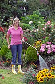 WOMAN WATERING FLOWERS IN GARDEN BED