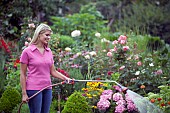 WOMAN WATERING FLOWERS IN GARDEN BED