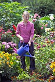 WOMAN WATERING FLOWERS IN GARDEN BED WITH WATERING CAN