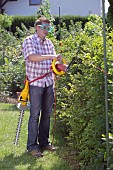 PERSON CUTTING PRUNING HEDGES WITH ELECTRIC TRIMMER