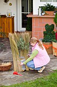 WINTER PROTECTION OF TENDER PLANTS.  LADY WRAPPING OLEA EUROPAEA (OLIVE) STANDARD CONTAINER TO PROTECT ROOTS WITH BUBBLE WRAP FOR INSULATION. DECORATIVE GRASS /REED  ROLL WRAPPED AROUND FINISHED WITH STRAW MULCH FOR EXTRA INSULATION.