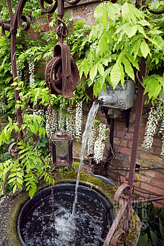 OLD_IRON_WATER_FEATURE_WITH_WISTERIA_SINENSIS_ALBA_GROWING_ON_WALL_IN_FONT_GARDEN_AT_WOLLERTON_OLD_H