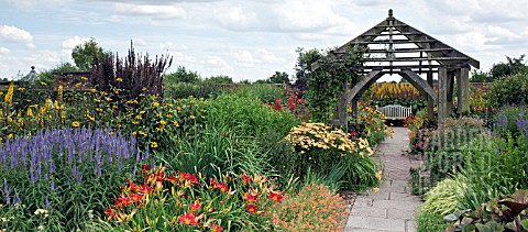 DEEP_BORDERS_OF_HOT_COLOURED_PERENNIALS_OAK_PERGOLA_AND_WOODEN_BENCH_AT_WOLLERTON_OLD_HALL