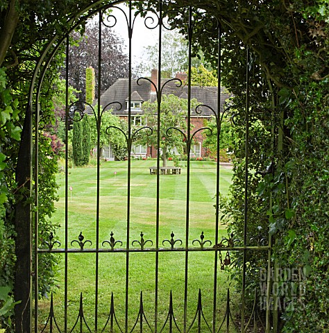 LOOKING_AT_GARDEN_AND_HOUSE_THROUGH_WROUGHT_IRON_GATE_AT_YARLET_HOUSE_STAFFORDSHIRE